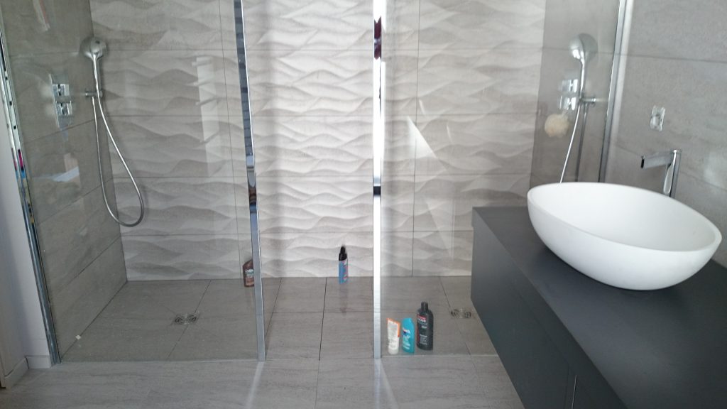Salle de douche moderne tons beige et gris avec lavabo blanc posé sur meuble gris et paroi de douche transparente mis en place par AG2P