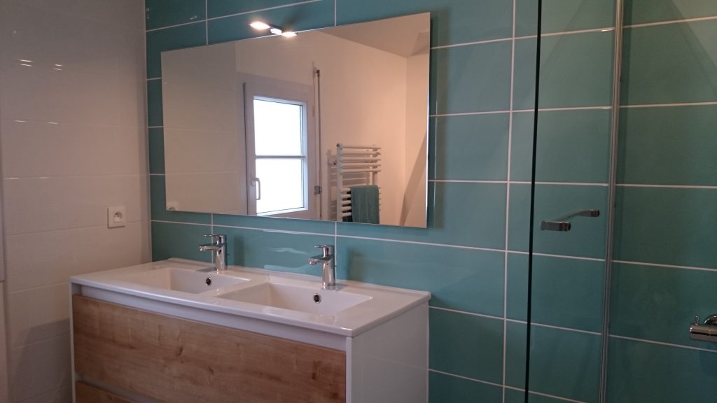 Salle de bain faiencée et installée par AG2P expert en plomberie et chauffage à Nantes. Grand miroir, meuble double vasque blanc et bois, faïence bleu clair
